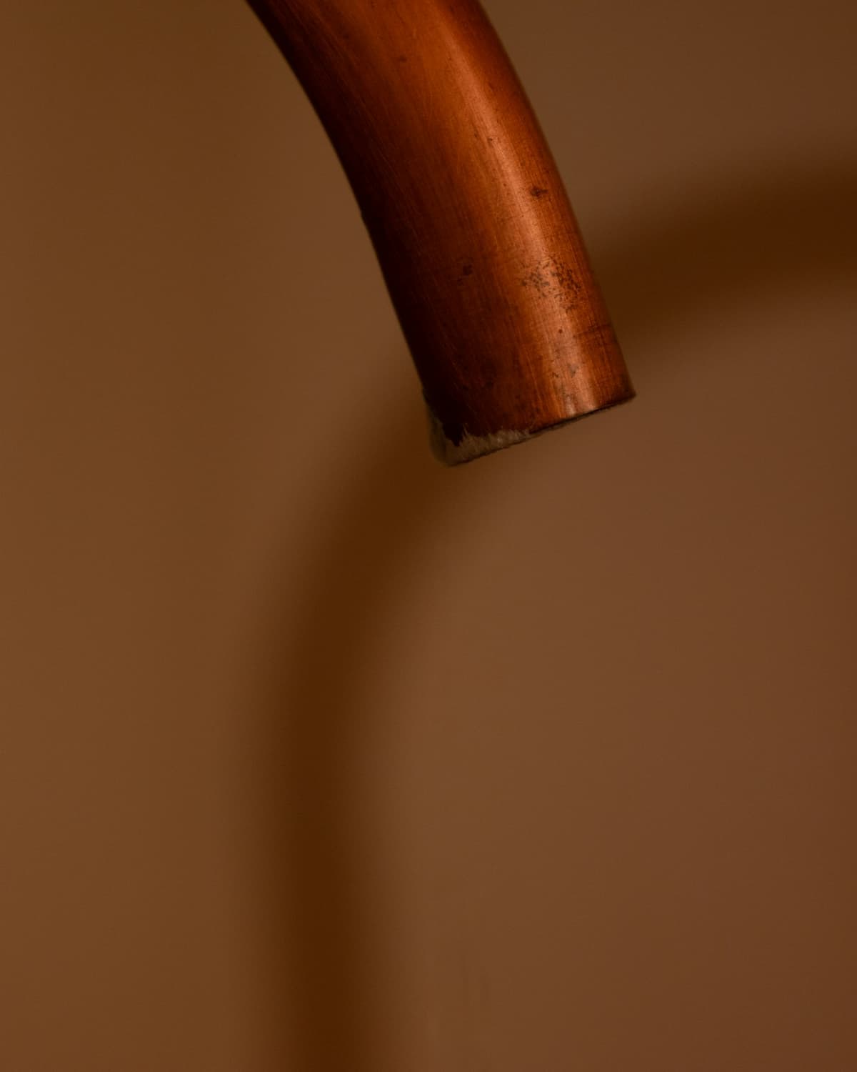 Close view of a bent copper pipe end against a warm, softly blurred background